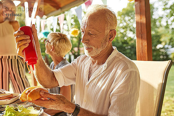 Älterer Mann bereitet einen Hot Dog auf einer Gartenparty zu