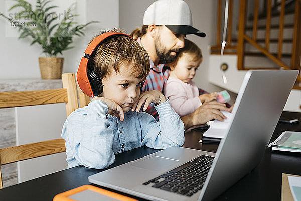 Vater arbeitet zu Hause und benutzt einen Laptop mit seinen Kindern auf dem Schoß