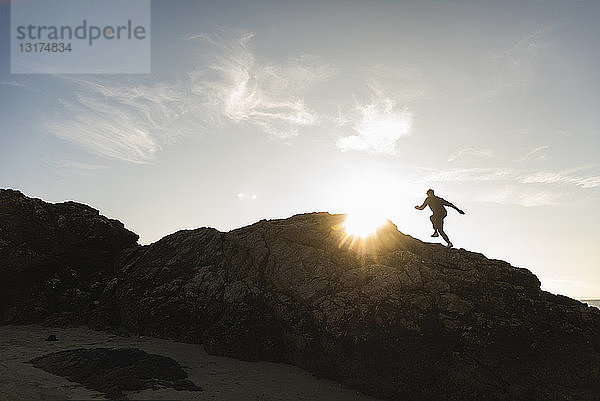 Frankreich  Bretagne  junger Mann rennt bei Sonnenuntergang auf einem Felsen