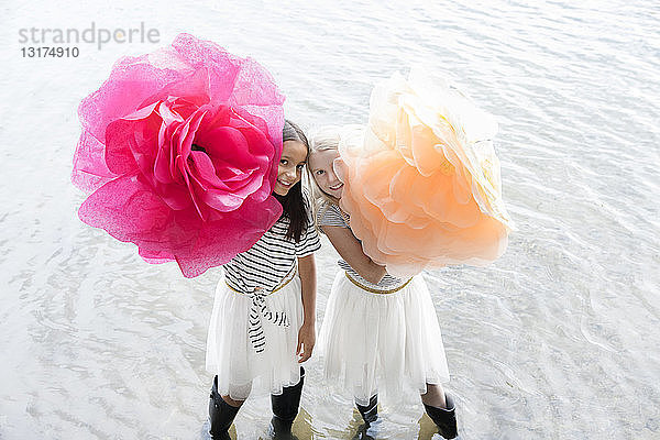 Zwei Mädchen stehen in einem See mit zwei überdimensionalen künstlichen Blumen
