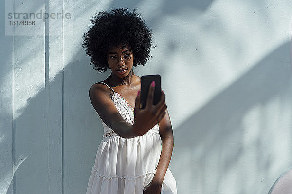 Junge Frau in weißem Kleid  die einen Selfie an einer Wand macht