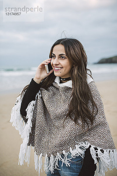 Porträt einer lächelnden jungen Frau am Telefon am Strand