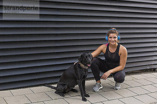 Porträt einer lächelnden jungen Frau mit Kopfhörer und ihrem Hund im Freien