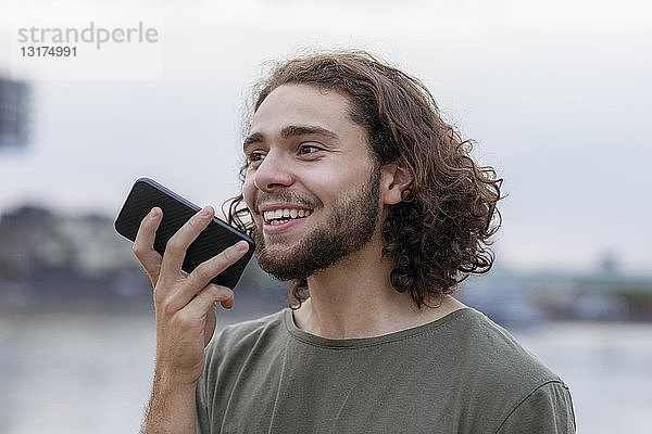Porträt eines glücklichen jungen Mannes  der sein Smartphone im Freien benutzt