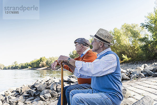 Zwei alte Freunde sitzen auf einem Baumstamm und beobachten den Fluss