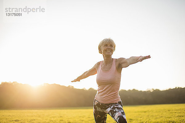 Ältere Frau macht Yoga auf einer ländlichen Wiese bei Sonnenuntergang