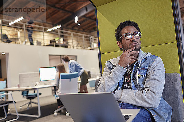 Junger Mann  der in einem kreativen Start-up-Unternehmen arbeitet und einen Laptop benutzt
