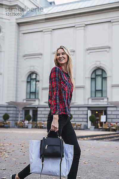 Porträt einer lächelnden jungen Frau mit Handtasche und Einkaufstasche im Gehen