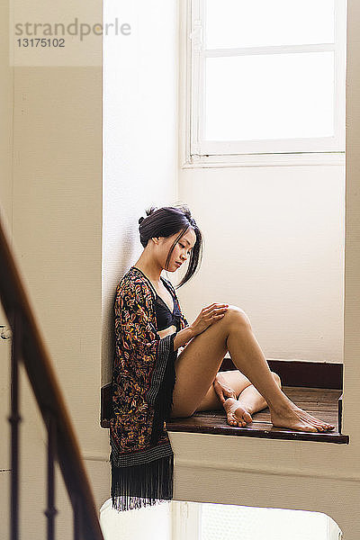 Attraktive junge Frau in Dessous  die in einer Nische am Fenster sitzt
