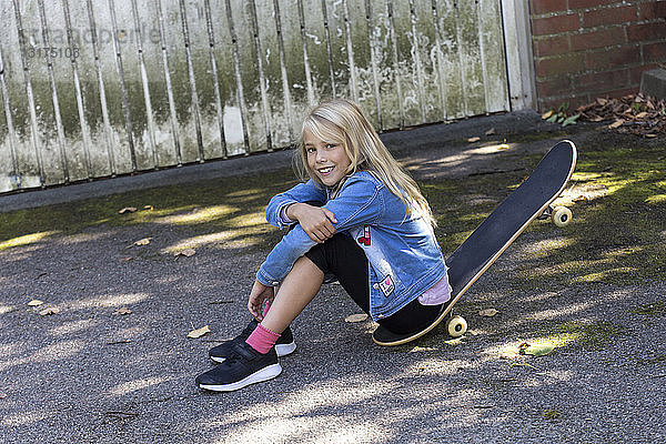 Porträt eines lächelnden blonden Mädchens  das im Freien auf seinem Skateboard sitzt