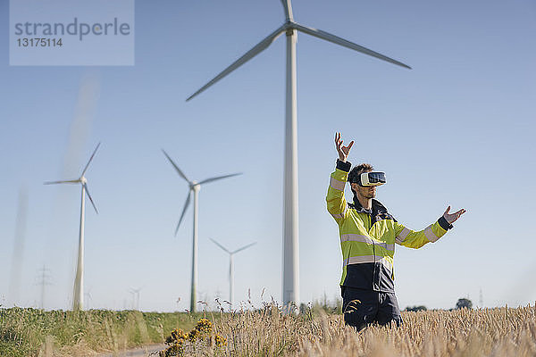 Ingenieur  der mit einer VR-Brille auf einem Feld in einem Windpark steht