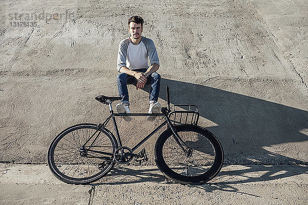 Junger Mann mit Pendler-Fixie-Fahrrad macht eine Pause und sitzt auf Betonmauer