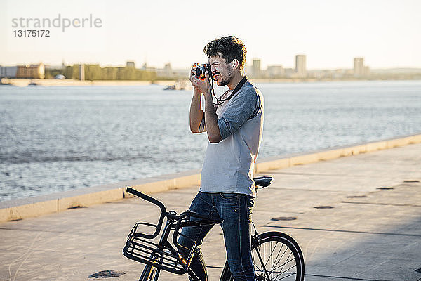 Junger Mann mit Pendler-Fixie-Fahrrad beim Fotografieren am Flussufer