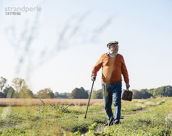 Älterer Mann mit Reisetasche  zu Fuß auf den Feldern