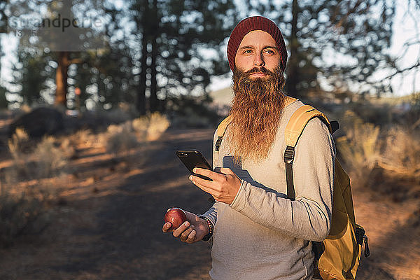 USA  Nordkalifornien  bärtiger Mann mit Handy und Apfel in einem Wald in der Nähe des Lassen Volcanic National Park