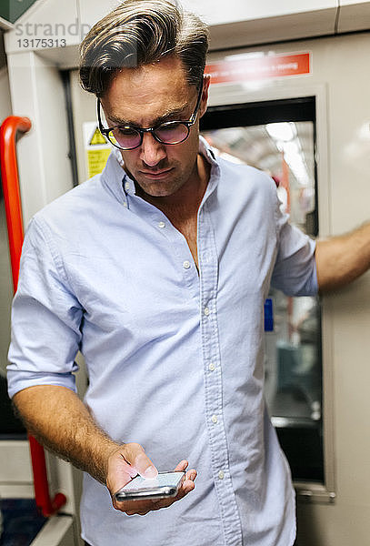 UK  London  Geschäftsmann in U-Bahn-Zug mit Blick auf Handy