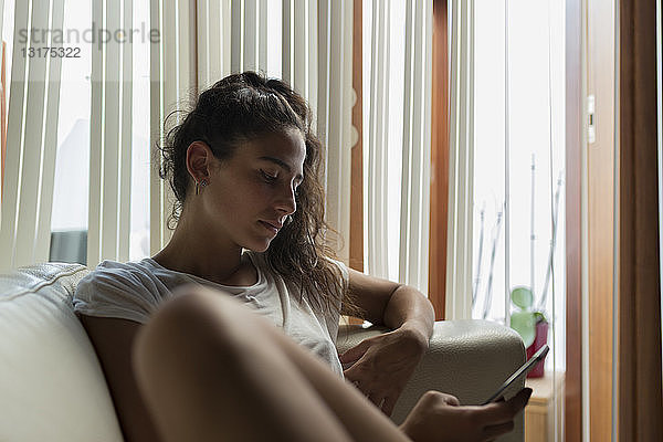 Junge Frau sitzt zu Hause auf dem Sofa und benutzt ein Smartphone