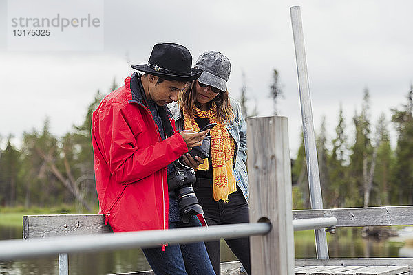 Finnland  Lappland  Ehepaar auf Steg an einem See mit Mobiltelefon