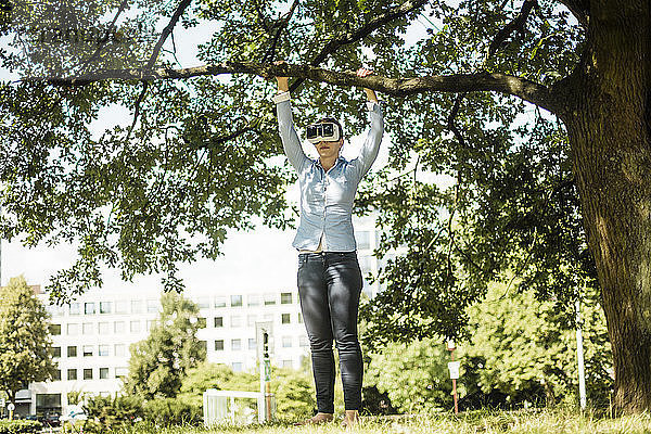 Frau im Stadtpark an einem Baum mit VR-Brille