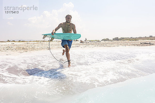 Junger Mann läuft mit seinem Surfbrett ins Meer