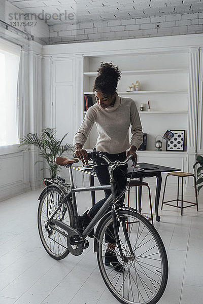 Mittlere erwachsene Frau  die ihr Heimbüro verlässt und ein Fahrrad schiebt