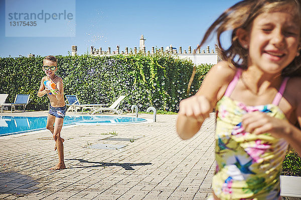 Junge mit Wasserpistole spritzt auf Mädchen am Pool