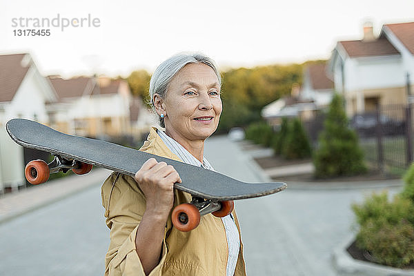 Porträt einer lächelnden älteren Frau mit Skateboard auf der Schulter