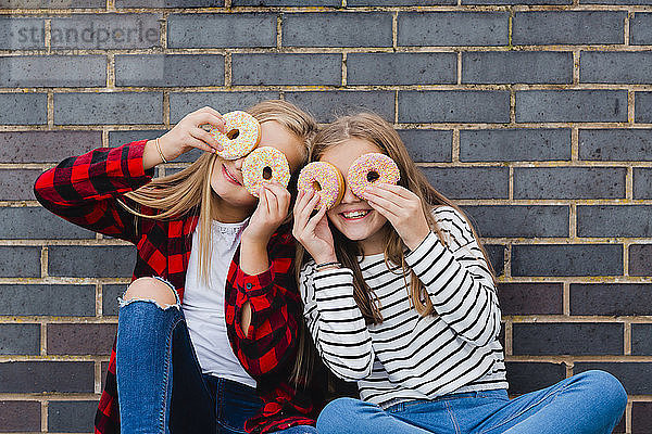 Zwei Mädchen amüsieren sich mit Doughnuts