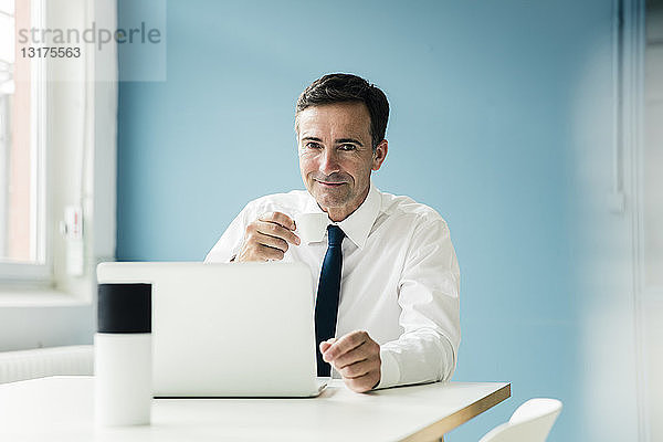 Porträt eines selbstbewussten Geschäftsmannes mit Laptop auf einem Tisch im Büro