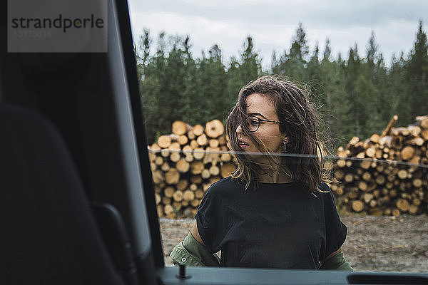 Junge Frau steht neben dem Auto neben einem Holzstapel