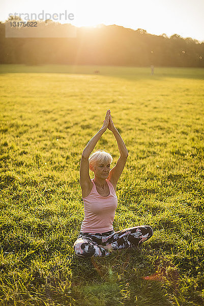 Ältere Frau macht Yoga auf einer ländlichen Wiese bei Sonnenuntergang