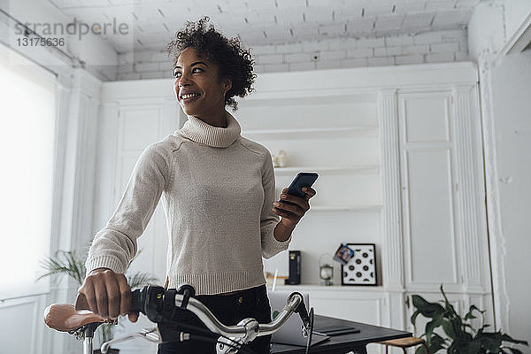 Mittlere erwachsene Frau  die ihr Heimbüro verlässt  Fahrrad schiebt  ein Smartphone benutzt
