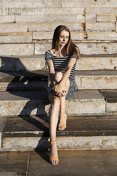 Porträt einer jungen Frau  die auf einer Treppe sitzt und den Sonnenuntergang genießt