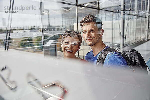 Porträt eines lächelnden Paares auf dem Flughafen  das aus dem Fenster schaut