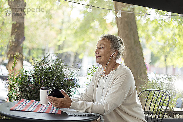 Ältere Frau in einem Café im Freien mit Handy und Kopfhörern