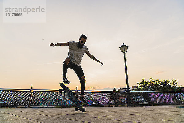 Junger Mann macht in der Stadt bei Sonnenuntergang einen Skateboardtrick