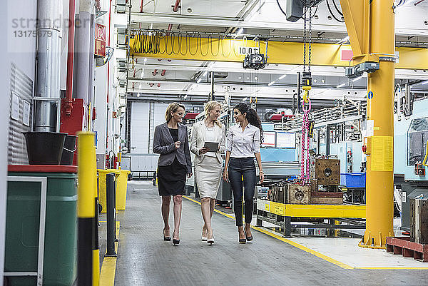 Drei Frauen mit Tabletten gehen und sprechen in der Fabrikhalle