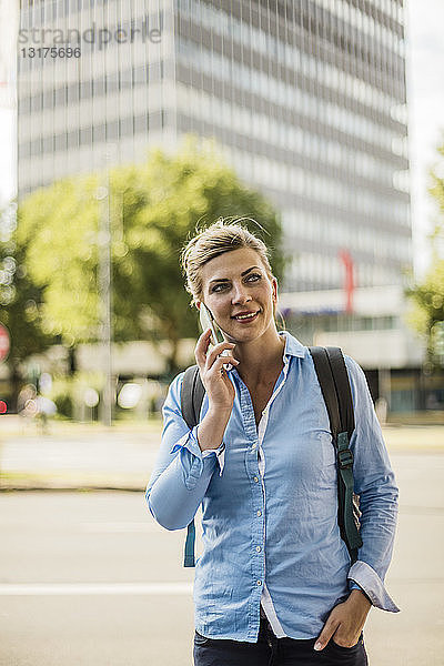 Lächelnde Frau mit Rucksack in der Stadt beim Telefonieren