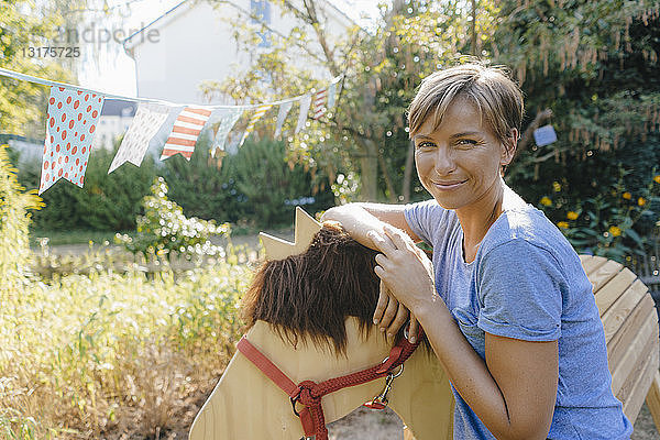 Bildnis einer lächelnden Frau mit Holzpferd im Garten