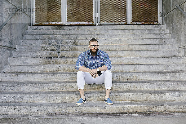 Porträt eines bärtigen Hipster-Geschäftsmannes mit Smartphone auf der Treppe sitzend