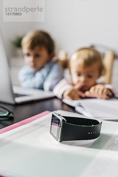 Smartwatch auf einem Schreibtisch  im Hintergrund Kinder mit Laptop