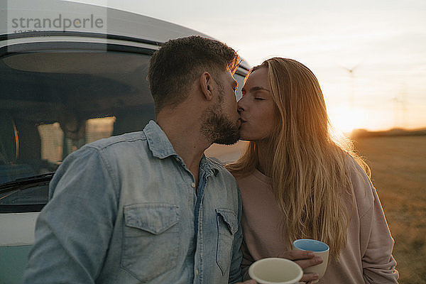 Junges Paar küsst sich am Wohnmobil in ländlicher Landschaft