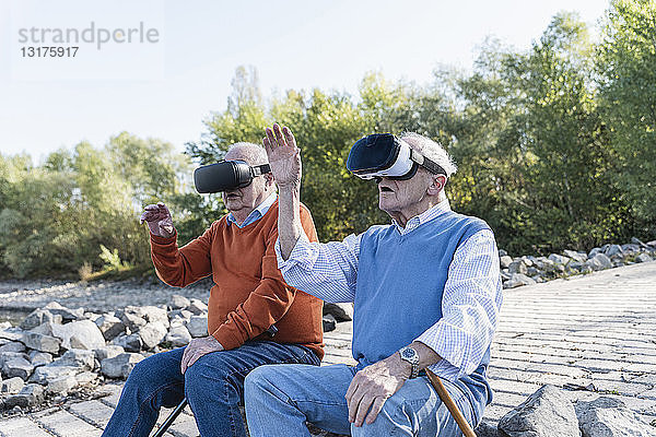 Zwei alte Freunde sitzen am Flussufer und tragen VR-Brillen