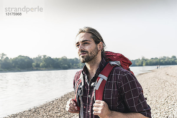 Selbstbewusster junger Mann mit Rucksack am Flussufer