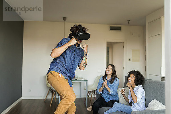 Zwei Frauen ermutigen Männer  zu Hause mit VR-Brillen zu spielen