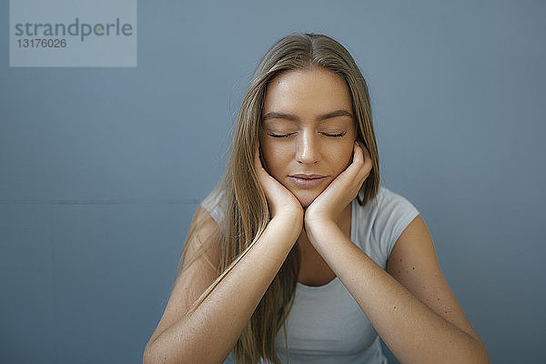 Porträt einer jungen Frau mit geschlossenen Augen und entspanntem Kopf in den Händen