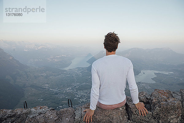 Schweiz  Grosse Mythen  junger Mann auf einer Wanderung  der bei Sonnenaufgang auf einem Felsen sitzt