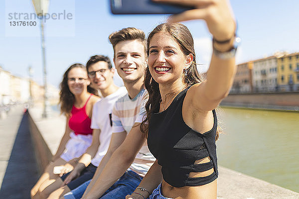 Italien  Pisa  eine Gruppe von vier glücklichen Freunden sitzt auf einer Mauer entlang des Arno und macht ein Selfie
