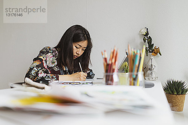 Illustratorin malt am Arbeitstisch in einem Atelier