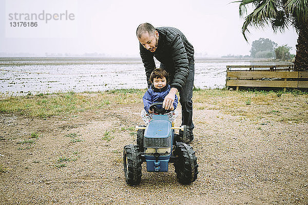 Vater hilft einem kleinen Mädchen  einen Spielzeugtraktor neben den Reisfeldern zu fahren